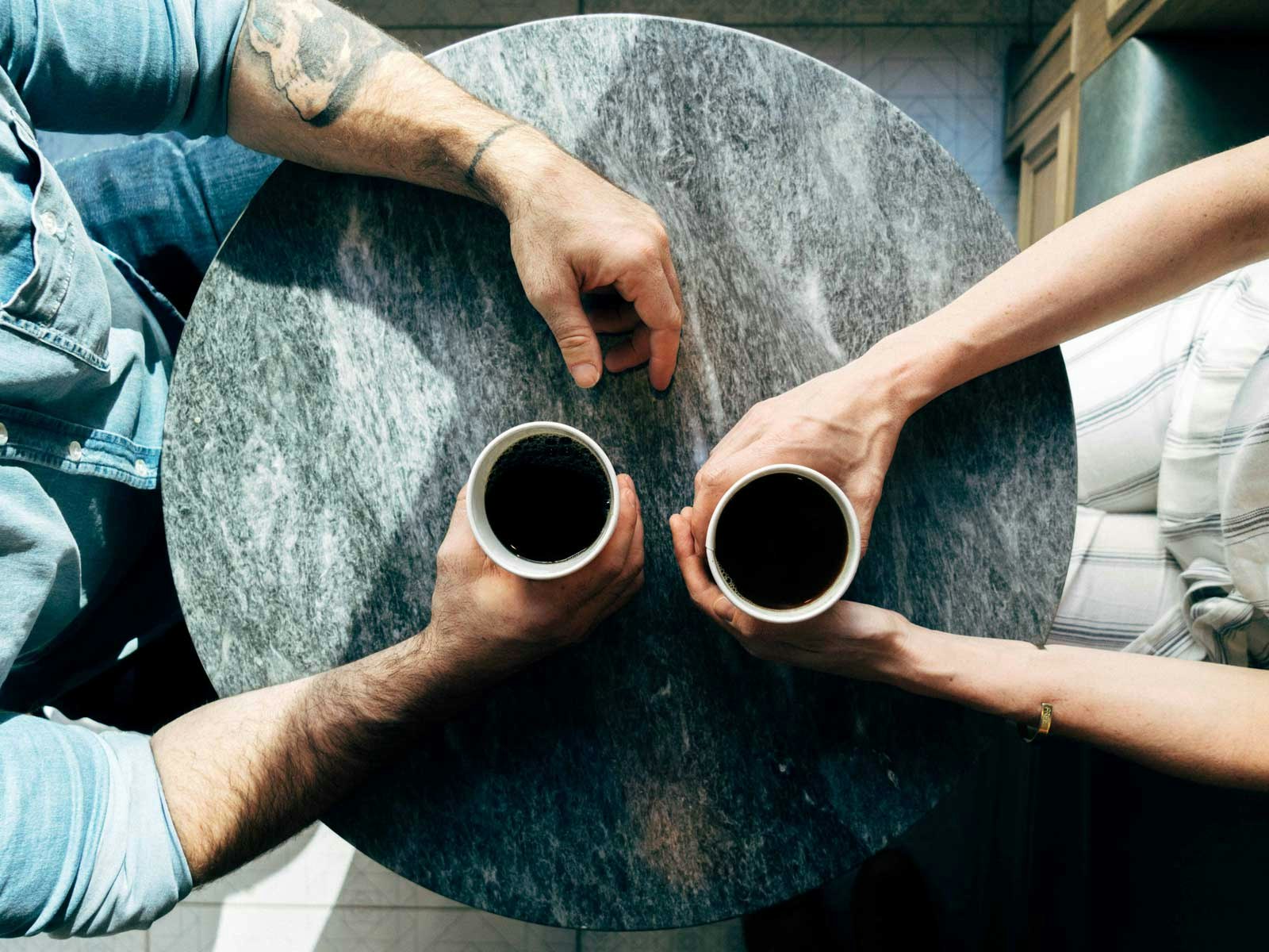 Two people sit at a table with mugs of coffee.